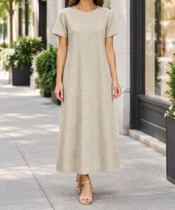 Woman wearing a beige linen t-shirt dress and sneakers on a city sidewalk, shown from the neck down