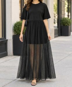 Woman wearing a black t-shirt dress with mesh skirt and sneakers on a city street, shown from the neck down