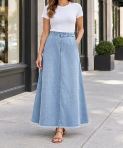 Woman wearing a light wash elastic waist denim skirt with sneakers on a city sidewalk, framed from the neck down