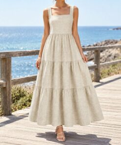 Woman wearing an oatmeal linen tiered summer dress walking on a sunny beach, seen from the shoulders down
