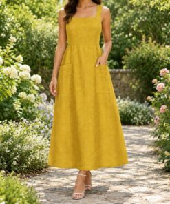 Woman in a mustard linen pinafore dress over a white tee in a vegetable garden, shown from the neck down